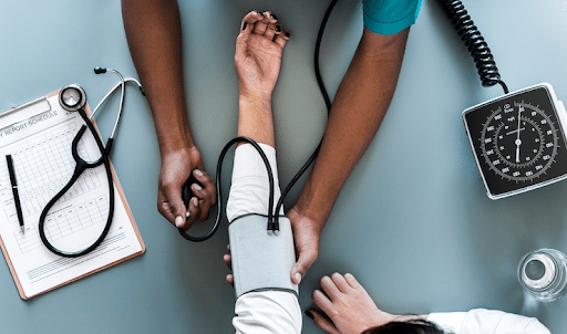 Imagem de um braço de uma paciente sendo consultada por um médico que está medindo sua pressão para simbolizar o Dia do Médico