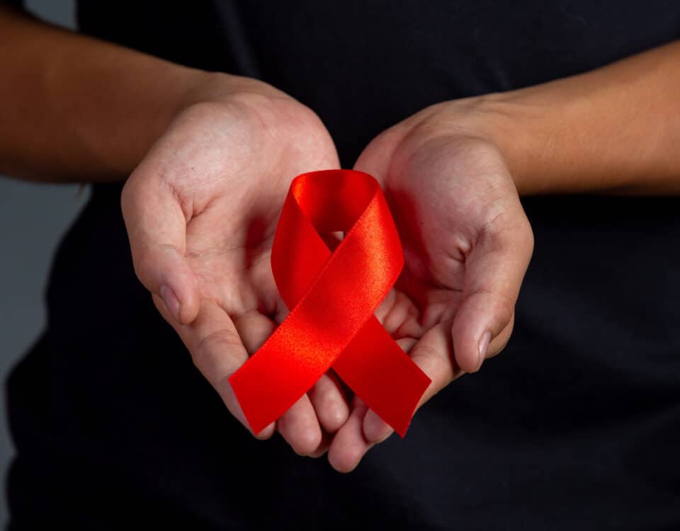 Imagem de duas mãos segurando uma fita vermelha para simbolizar como a AIDS é transmitida